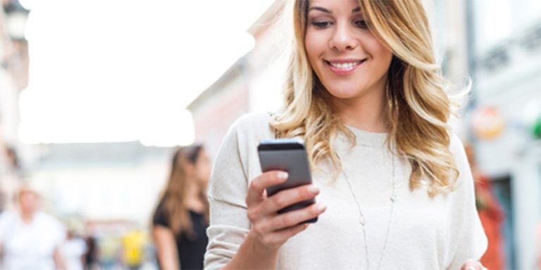 Frau schaut lächelnd auf Ihr Handy